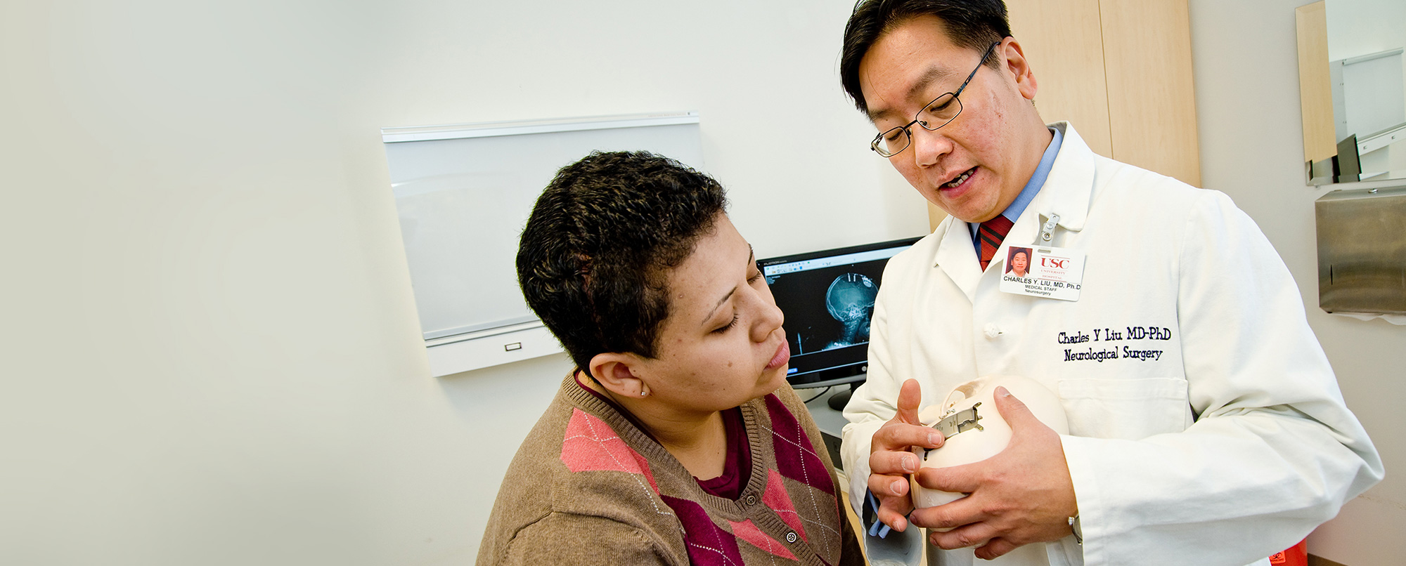 Charles Liu, MD, PhD, a Keck Medicine neurosurgeon, shows a female patient a model of a brain and skull