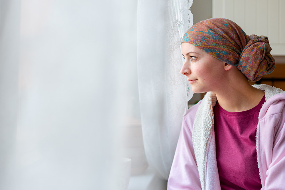 Woman treated for breast cancer sits at window.